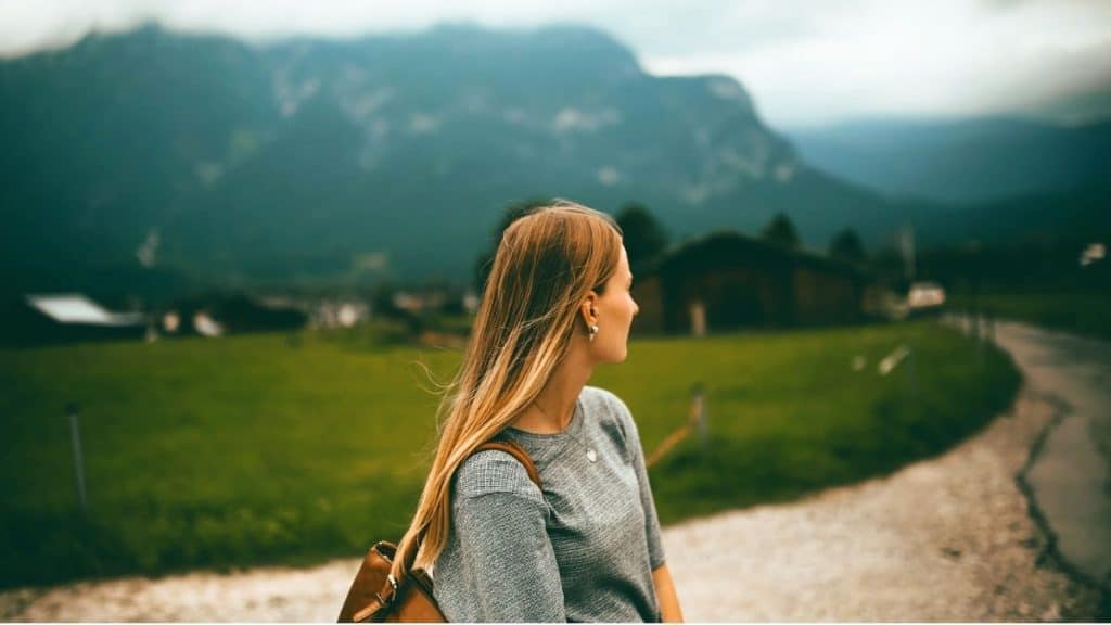 Young woman in a valley looking toward mountains from a country road