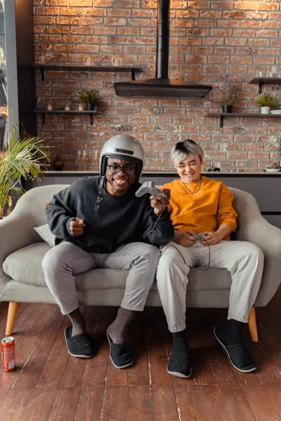 Two friends laughing and gaming together on a sofa at home