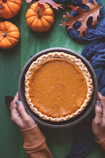 Homemade pumpkin pie surrounded by small pumpkins and autumn leaves