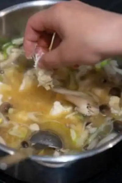 person's hand adding ingredients to a pot of homemade chicken soup