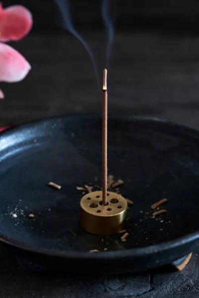 Burning incense stick in a small round brass holder with multiple-sized openings