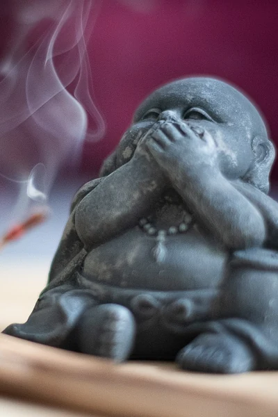 Laughing Buddha figurine beside a burning incense stick