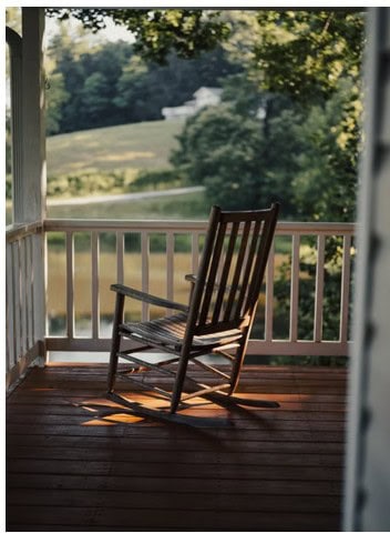 Wooden rocking chair on a country porch overlooking a large hilly yard
