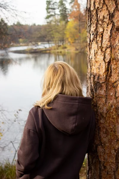 woman leaning against a big tree and looking at the creek