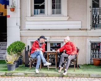 Two adults in jackets talking over coffee at an outdoor table