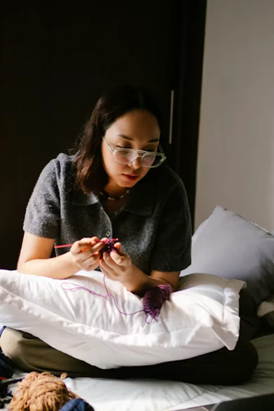Woman knitting while sitting comfortably on a bed