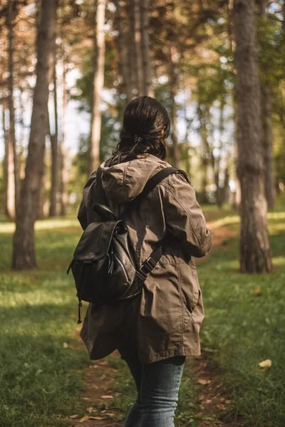 young woman with a backpack and jacket on walking through the park
